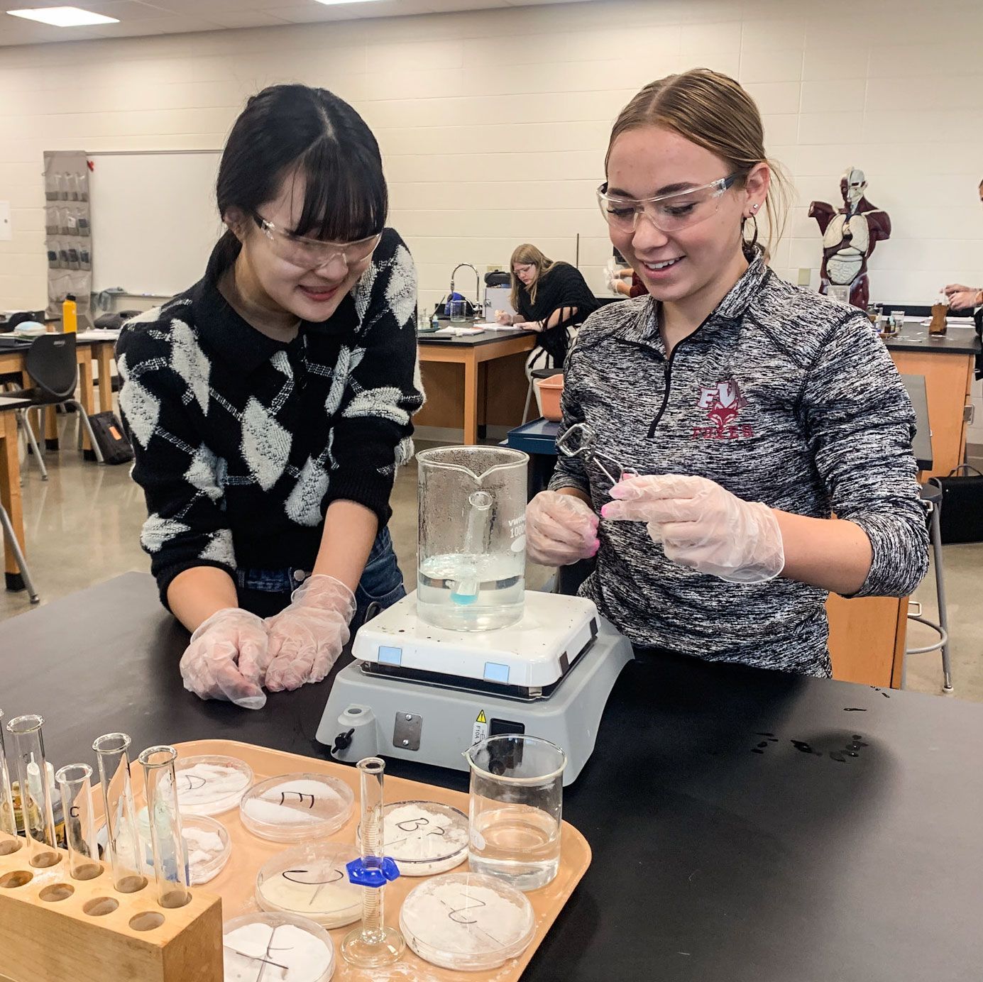 Two smiling female students in the bio lab, working on an experiment.