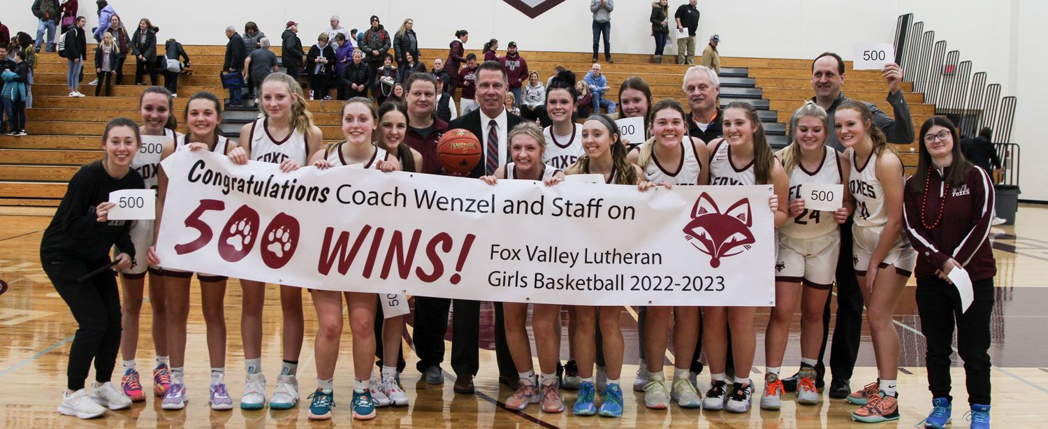 Basketball girls and Rev holding a congratulations sign after Rev wins his 500th game