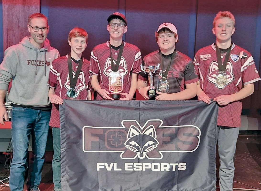 The four team members and their coach holding their trophy and their FOXES FVL ESPORTS banner at their State Tournament