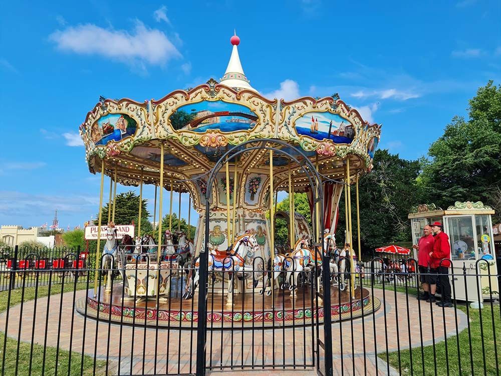 A merry go round is behind a fence in a park.