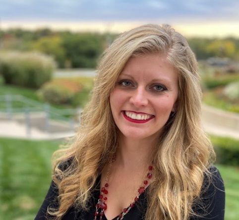 The woman is wearing a black shirt and a red necklace and smiling for the camera.