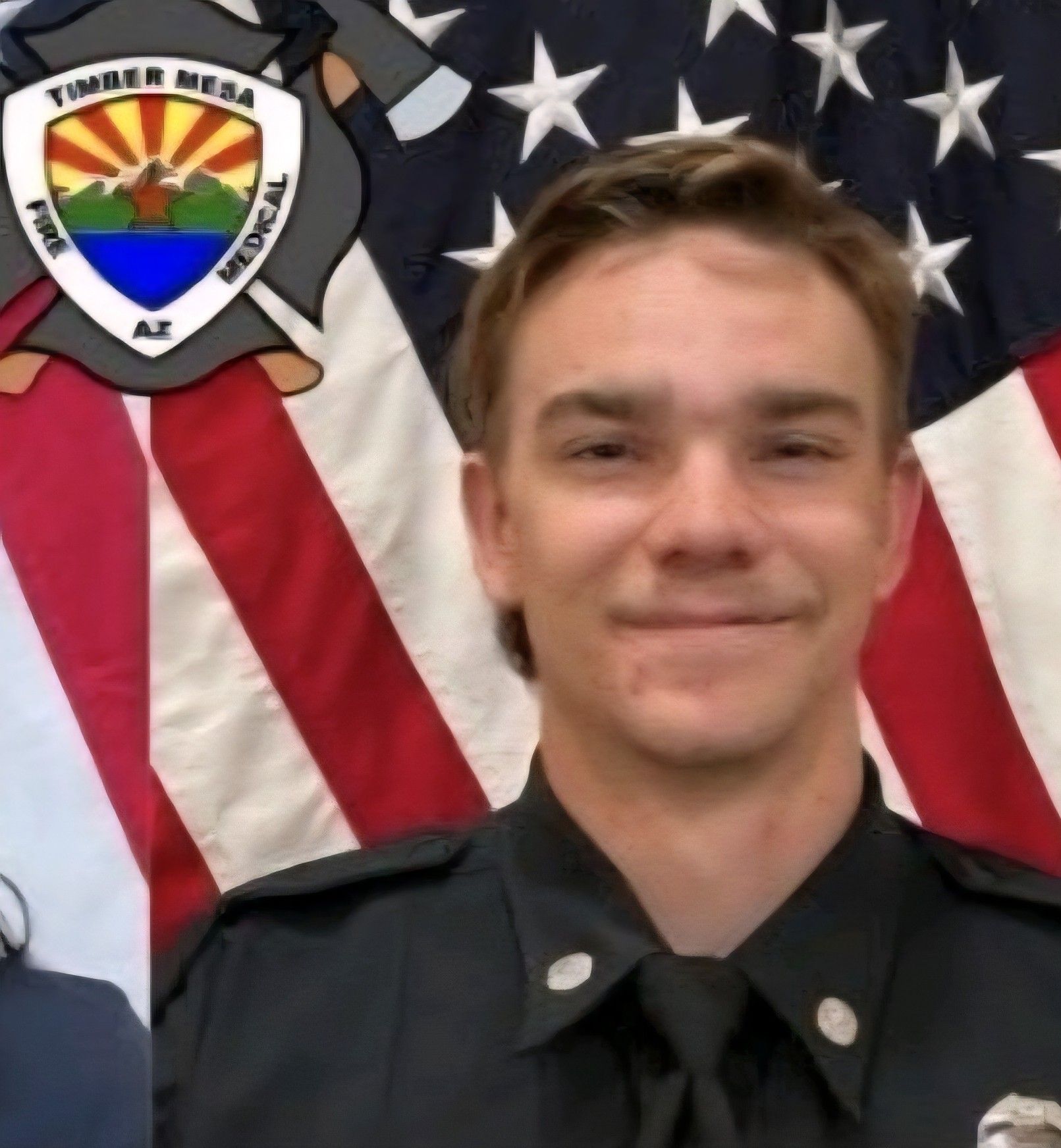 Firefighter in uniform, smiling, with American flag backdrop and Timber Mesa Fire Medical logo.