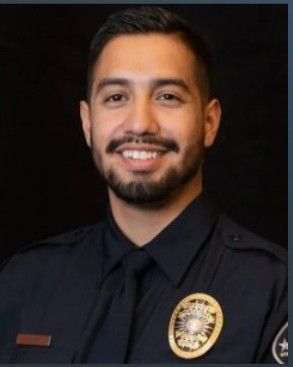 Smiling police officer with a dark beard, wearing a uniform.