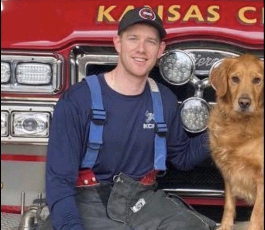 A man in a wheelchair is sitting next to a dog in front of a kansas city fire truck