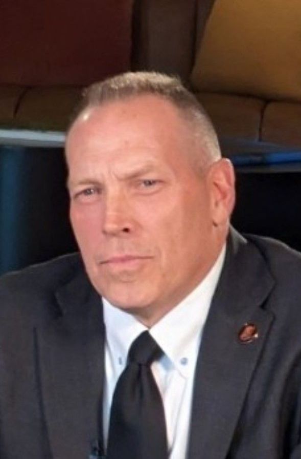 A man wearing a black sweater is smiling for the camera