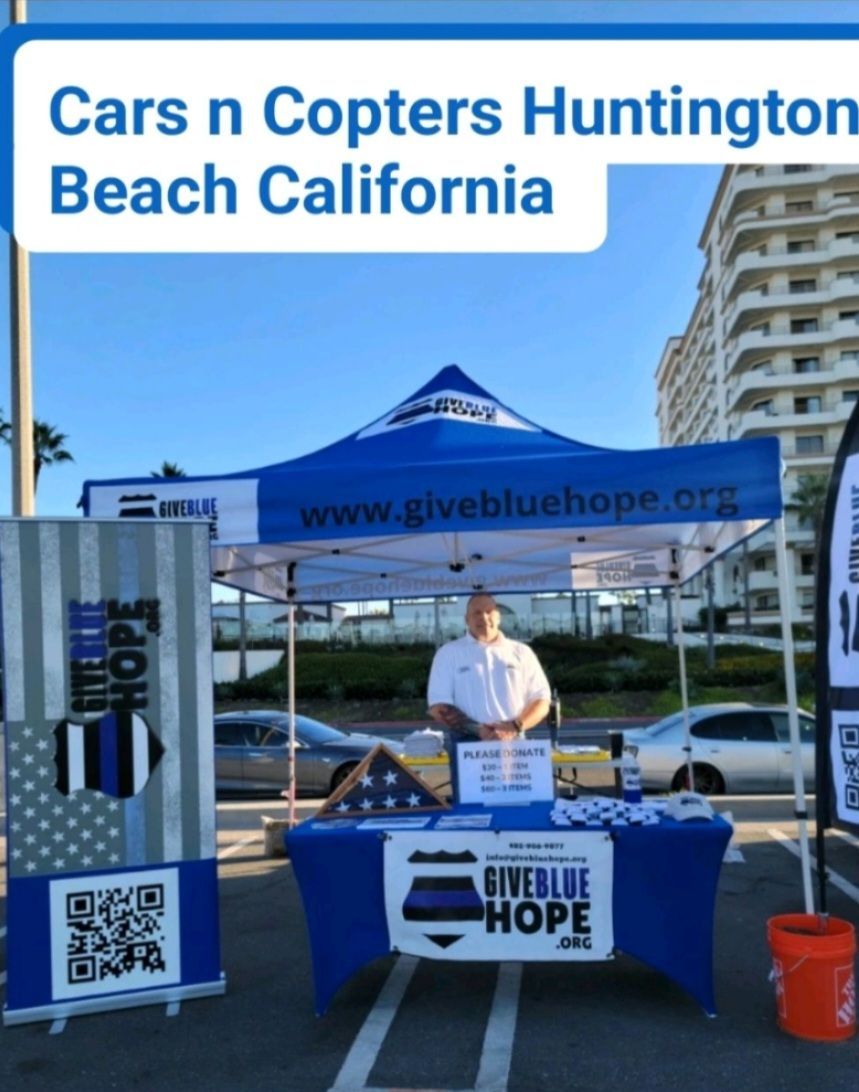 A man stands behind a table that says cars n copters huntington beach california