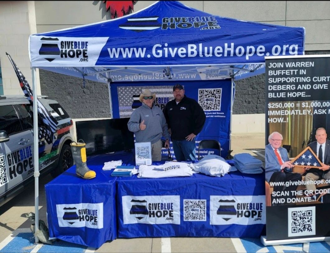 Two men standing under a blue tent that says givebluehope.org