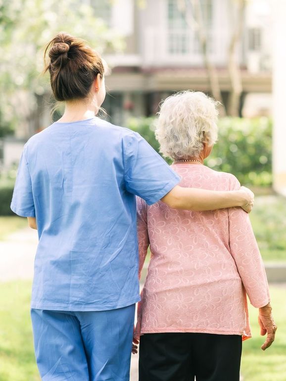 a nurse is walking with an elderly woman in a park .