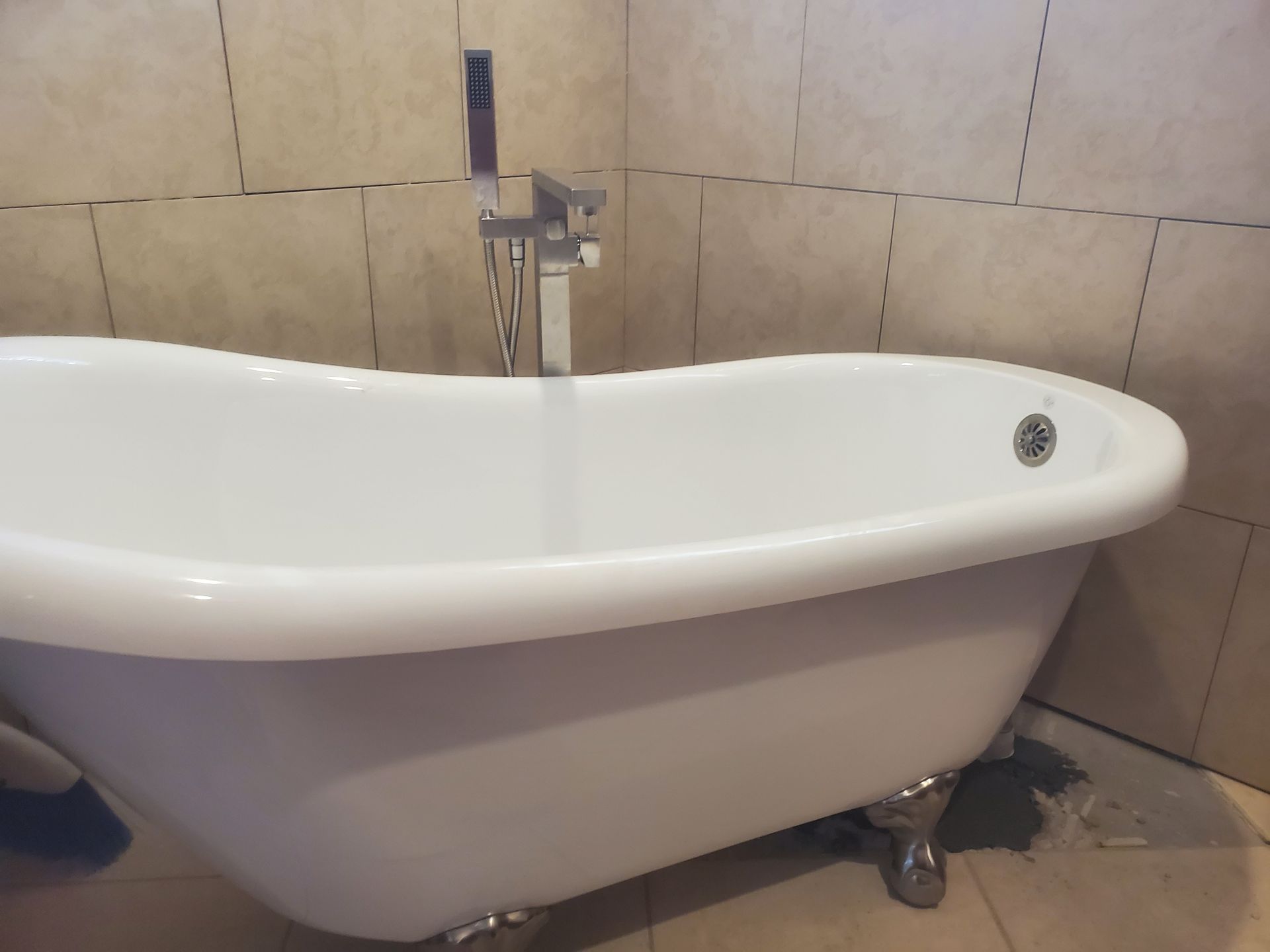 White clawfoot bathtub with chrome faucet against beige tile walls.