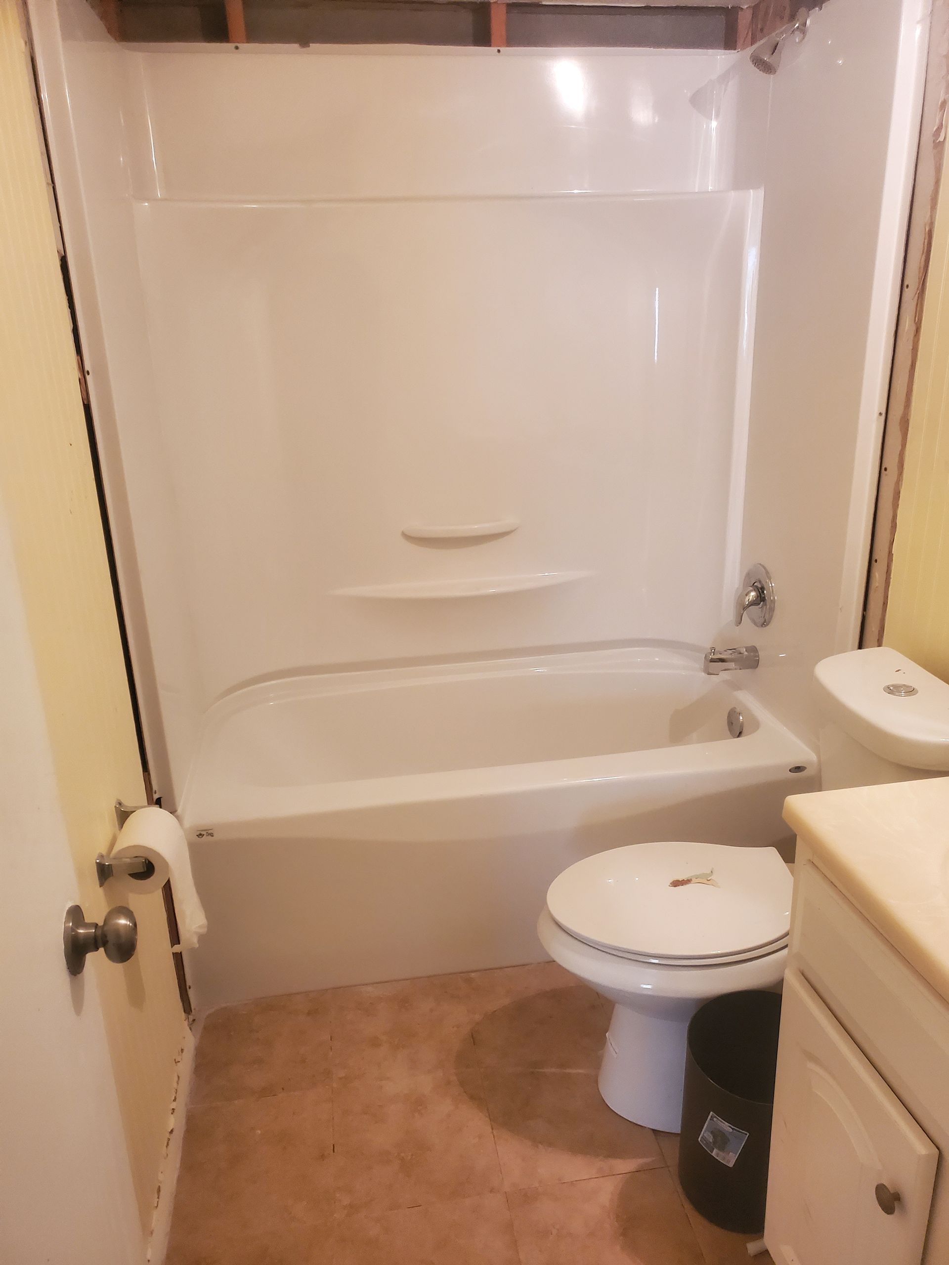 Bathroom with white tub/shower combo, toilet, and tan floor.