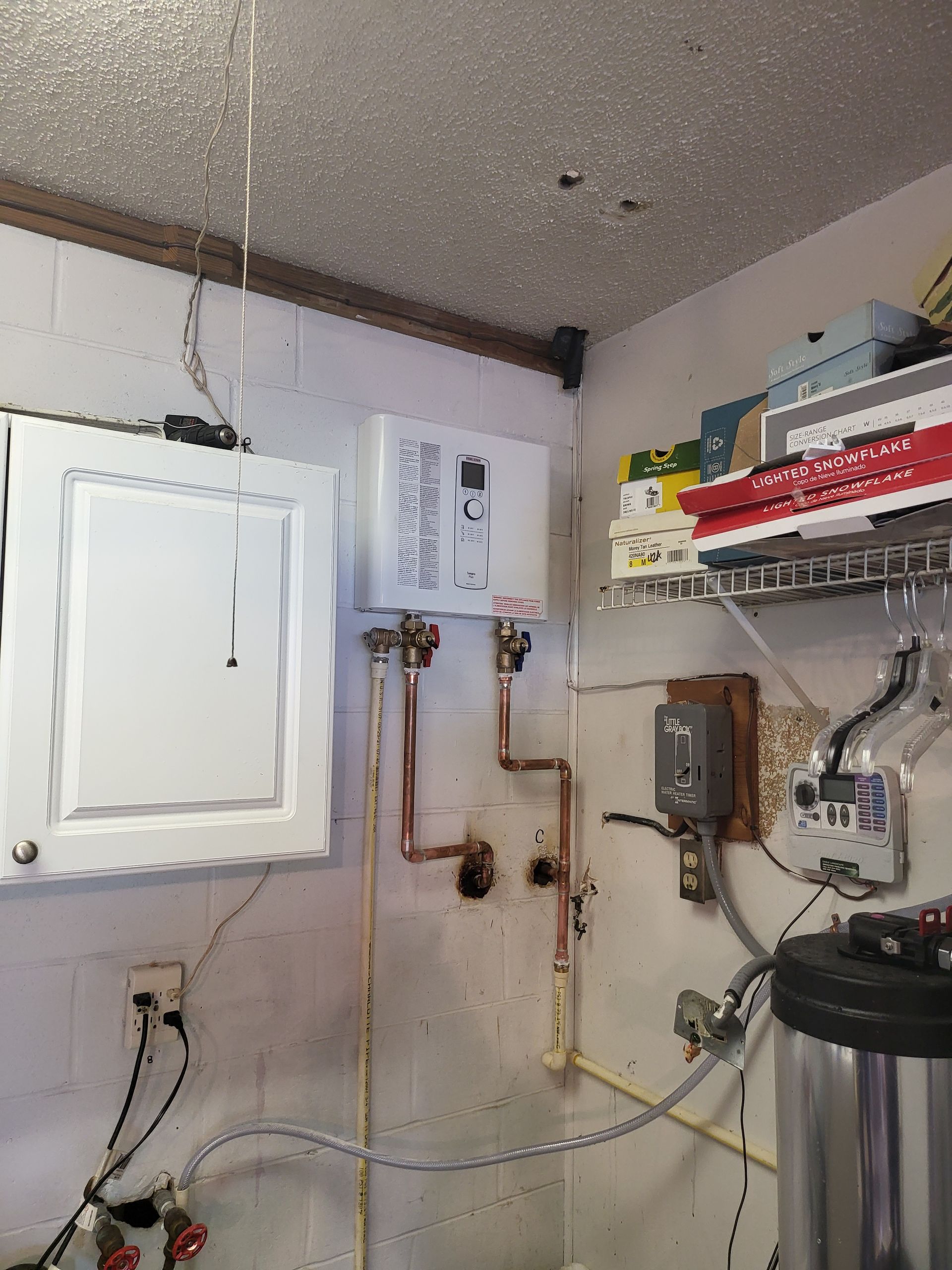 Water heater and related plumbing on a white brick wall.