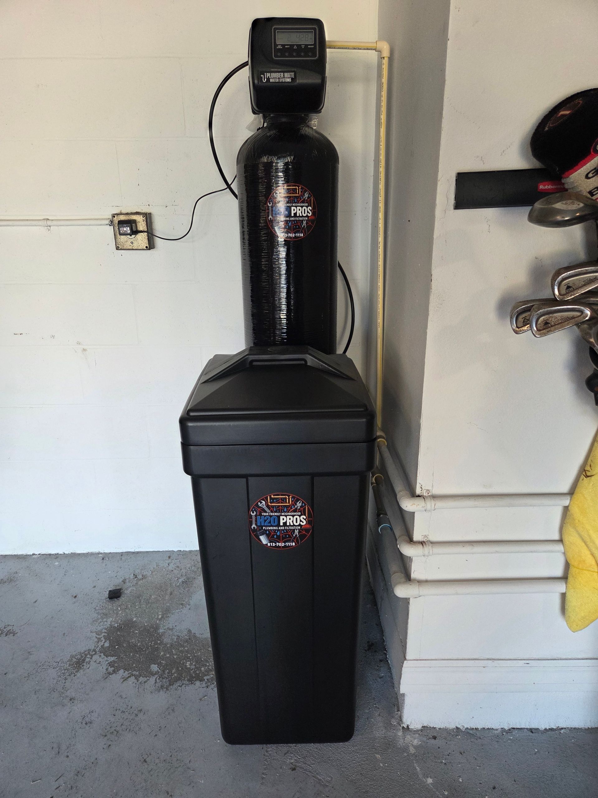 Black water softener system installed against a white wall in a garage.