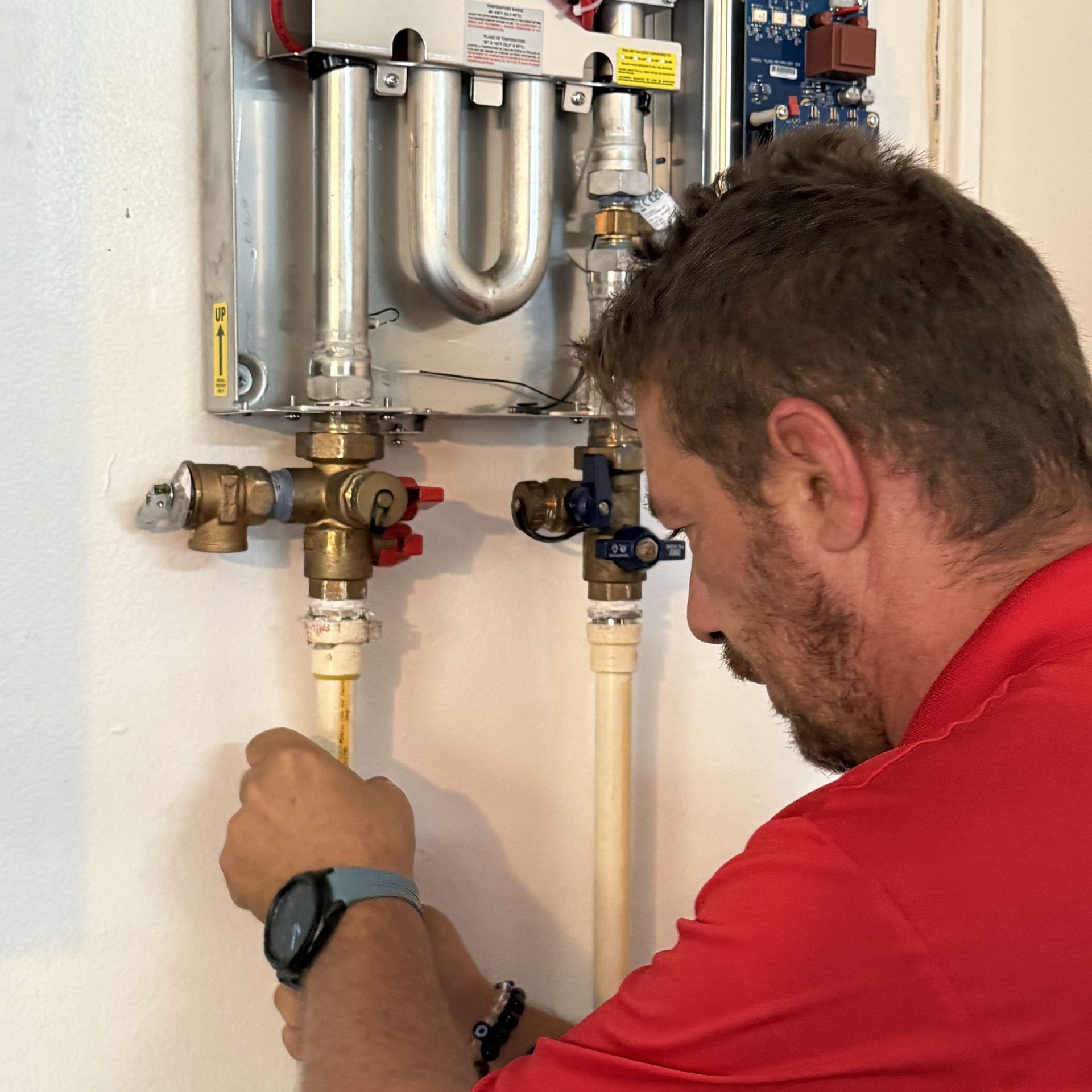 Man working on a water heater, inspecting pipes on a white wall.