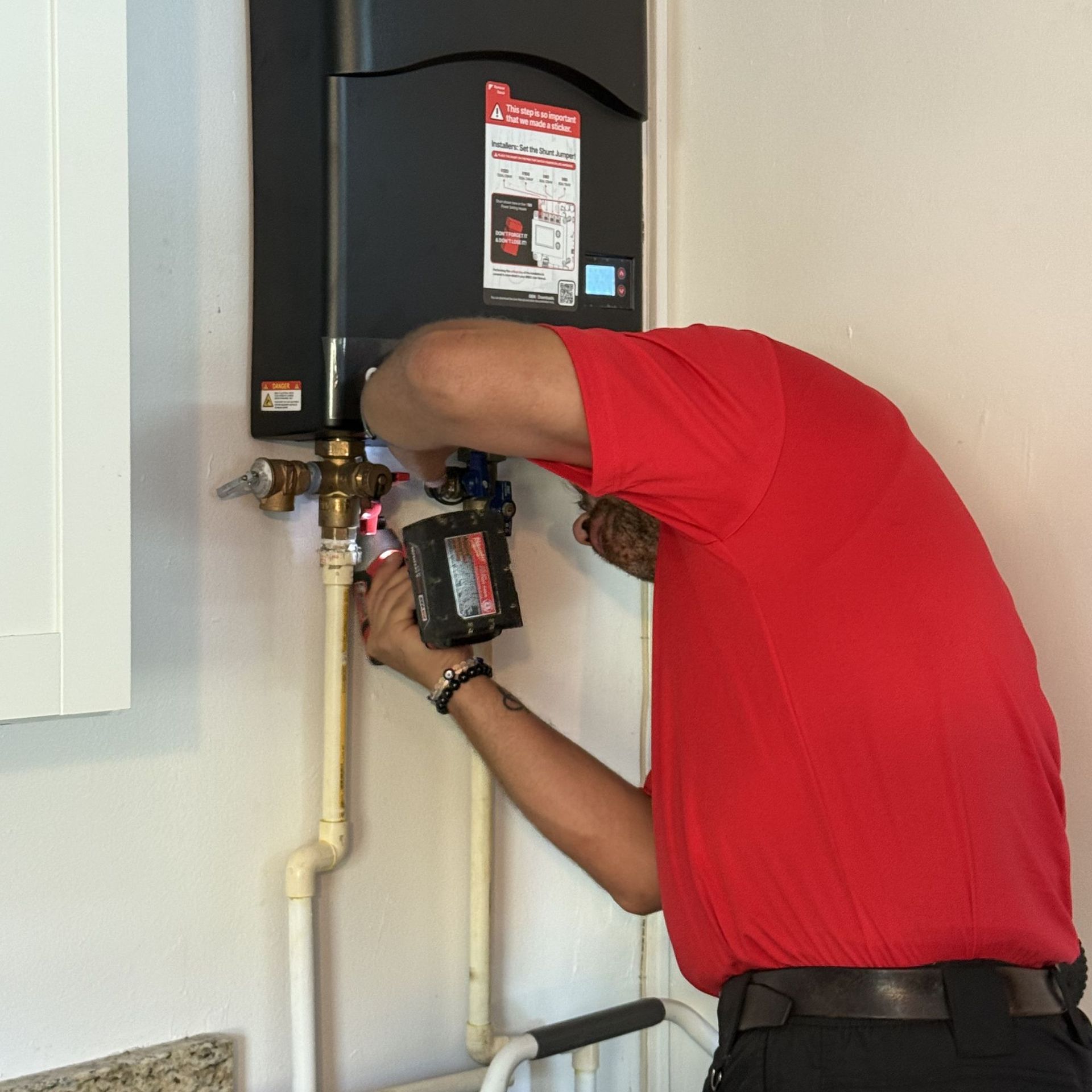 Plumber in a red shirt installing a water heater on a wall.
