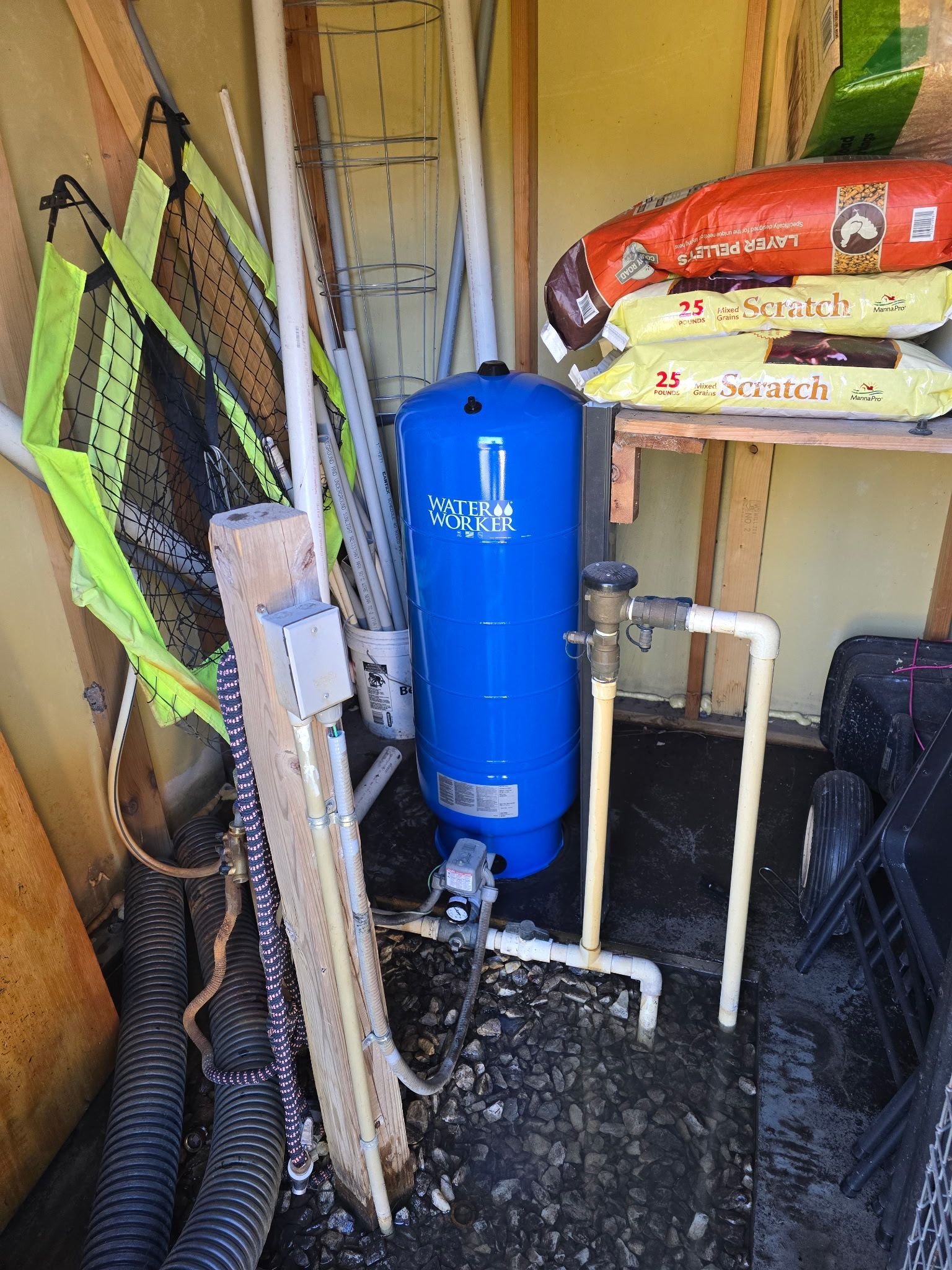 Blue water pressure tank inside a shed, with PVC pipes and various objects leaning against the walls.