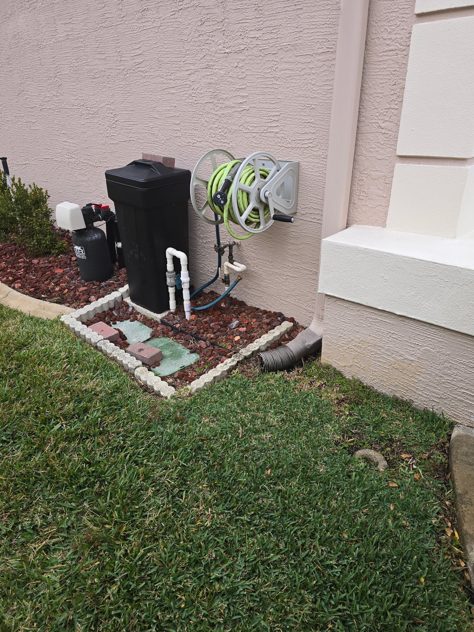 Outdoor water hose reel and equipment on a stucco building next to a lawn with red mulch.