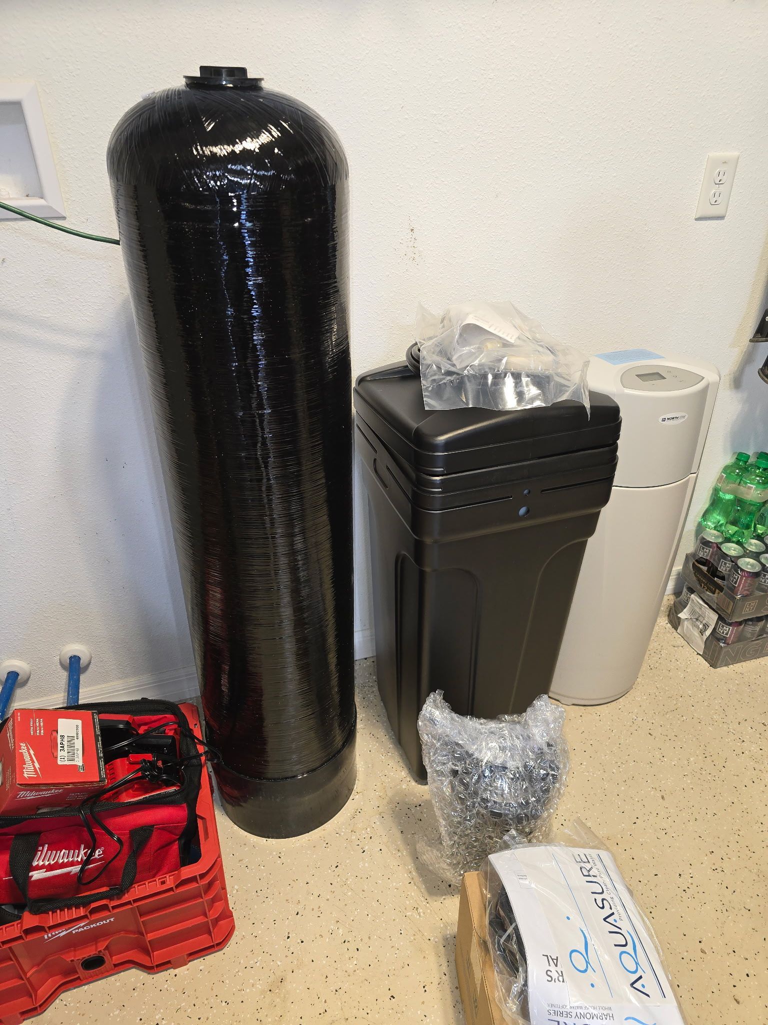 Water filtration system components: black tank, salt tank, and white container, indoors.