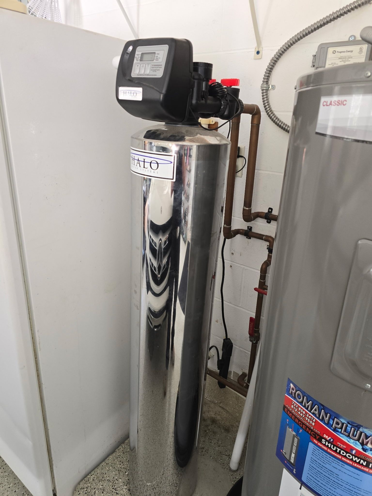 A tall, cylindrical water softener next to a hot water heater and a white refrigerator.