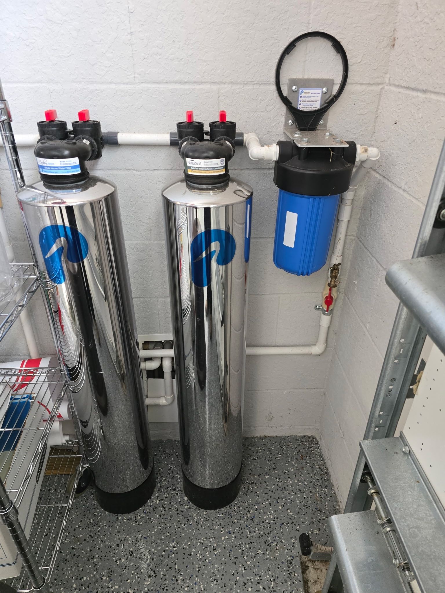 Water filtration system with three tanks and white PVC piping in a utility room.