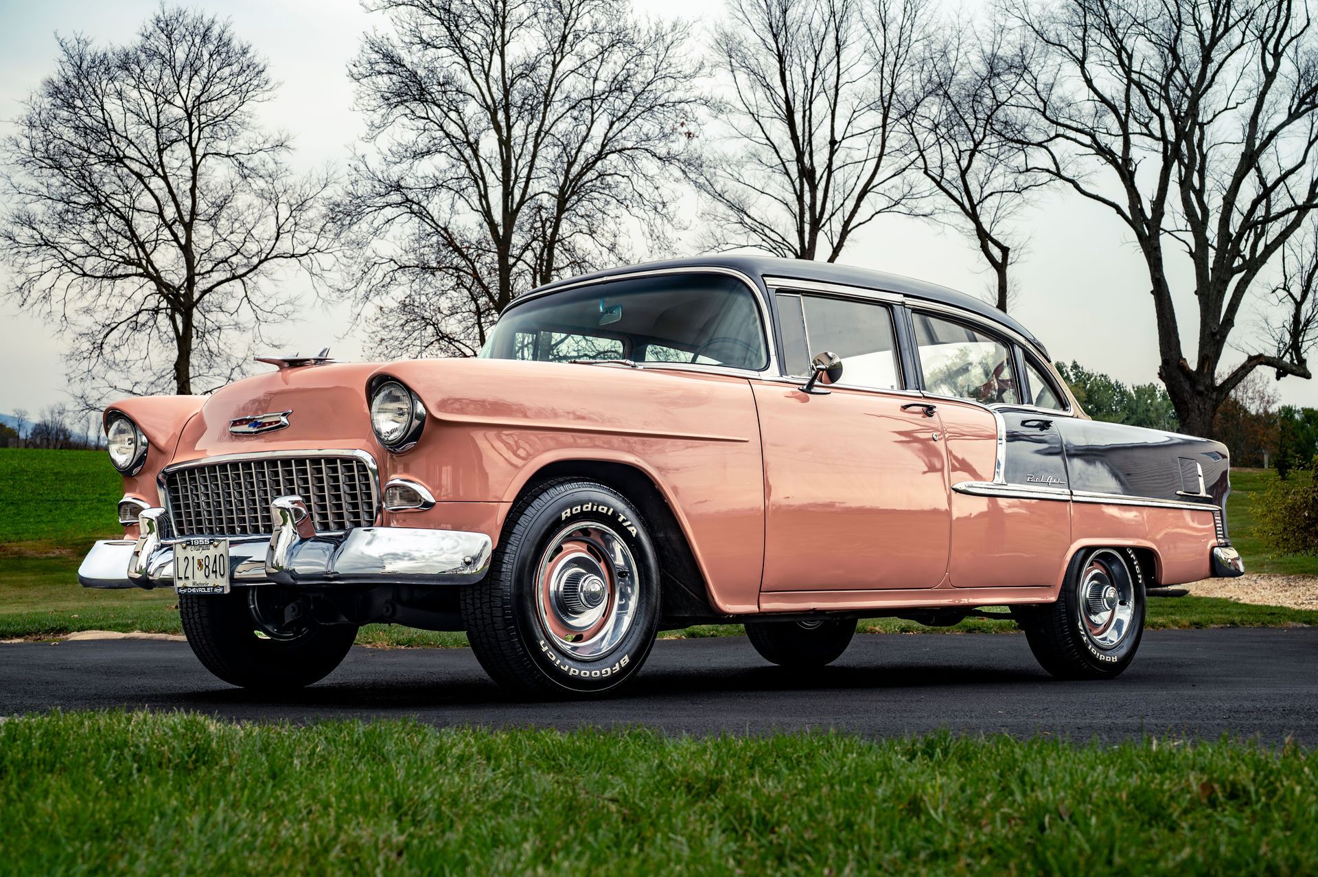 Pink vintage car parked on a road with leafless trees in the background