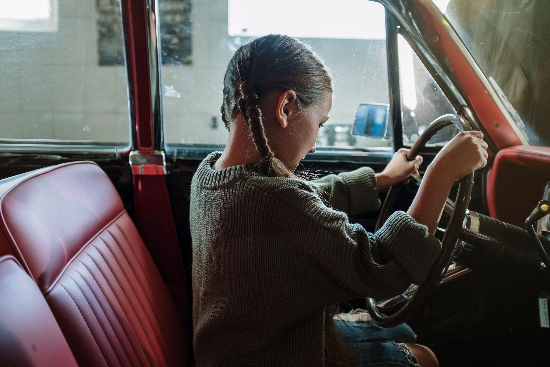 Person sitting in a red car, adjusting the steering wheel in the driver’s seat.