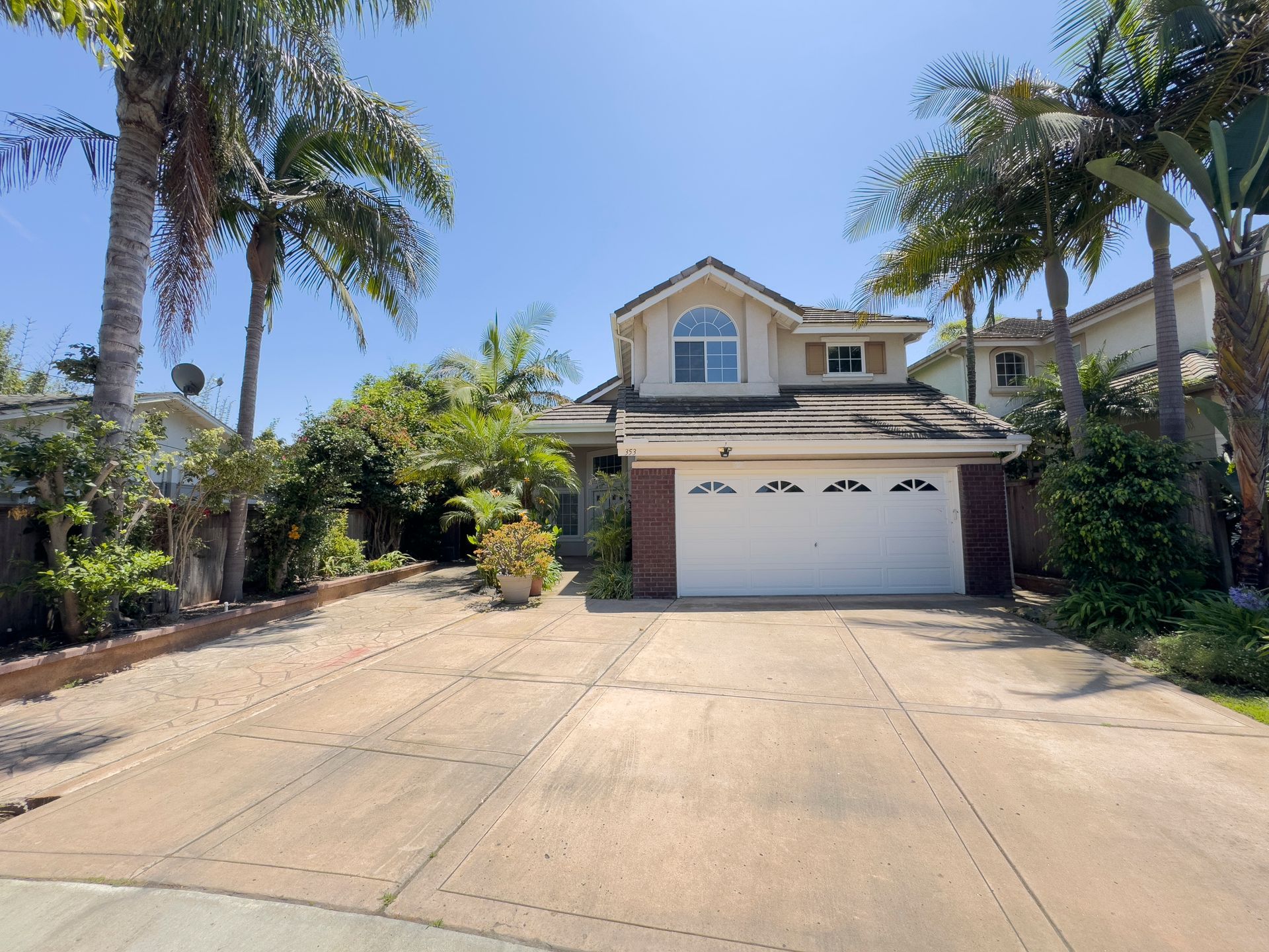 A house with a white garage door is surrounded by palm trees