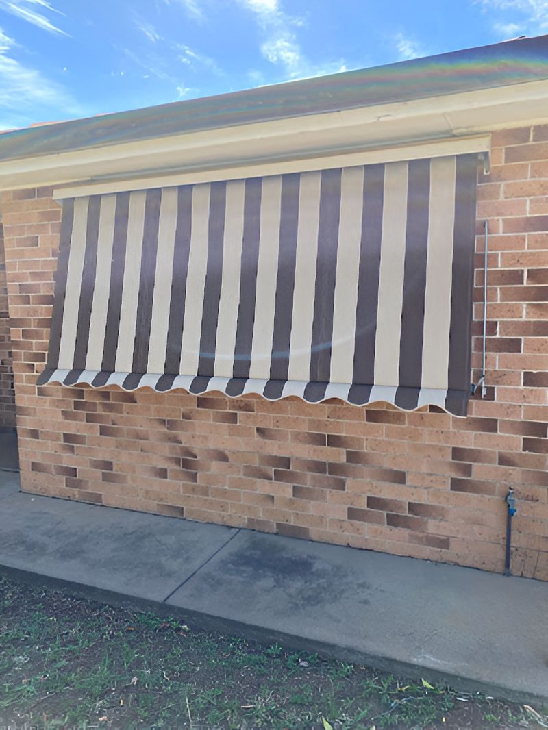 A Black and White Striped Awning is Hanging on the Side of a Brick Building — Tamworth Blinds & Awnings in Tamworth, NSW
