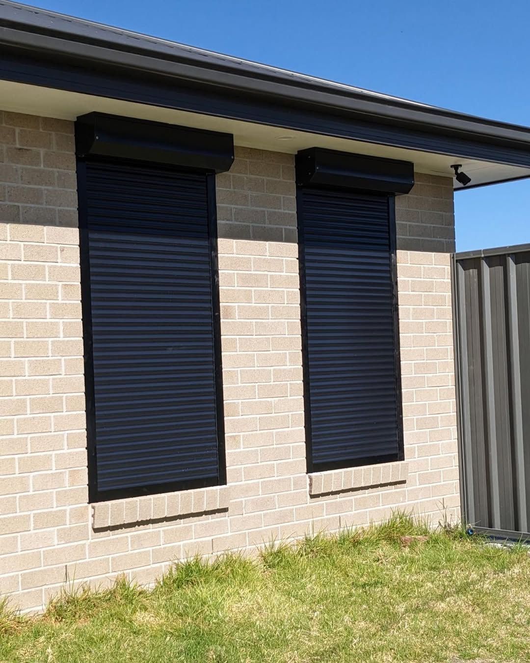 A Brick House With Two Black Roller Shutters on the Windows — Tamworth Blinds & Awnings in Narrabri, NSW