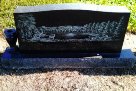 Black granite headstone featuring an etched landscape of a lake, forest, mountains, and wildlife, with a vase attached.