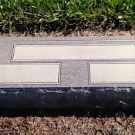 A grey granite grave marker with three blank rectangular panels, positioned on the ground against a grass background.