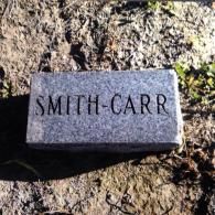 A gray, rectangular stone marker resting on the ground with the words 