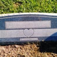 A blue granite headstone set in the grass, featuring a large engraved heart in the center and blank name plates.