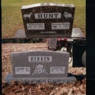 Two cemetery headstones, one brown and one grey, each engraved with a surname and names with dates.