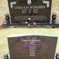 Two dark granite headstones in a cemetery; the top one is inscribed for Linda Kay McSpadden, the bottom one for her family.