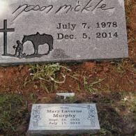 Two grave markers set in the ground, one larger featuring a cross and horse, the other smaller with decorative borders.