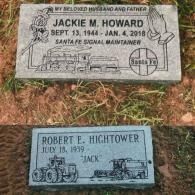 Two gray granite grave markers set in grass. Top: Jackie M. Howard, train imagery. Bottom: Robert E. Hightower, farm gear.