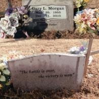 A grave marker for Gary L. Morgan with a plaque below it reading, 