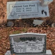 Two grave markers set in the ground, one for Conner Lee Pool and one for the Qualls family, on a field of dry leaves.