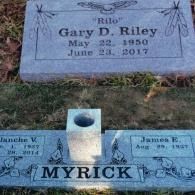 Two gray granite grave markers set in the grass; one for Gary D. Riley, the other for the Myrick family.