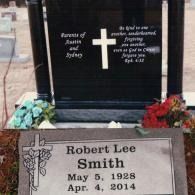 A gravestone for Robert Lee Smith (1928–2014) in front of a larger, upright black monument with a white cross and scripture.