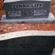 Two gray granite gravestones in a cemetery, with the name TUNNICLIFF and dates inscribed on the top stone.
