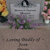 A grave marker for Howard Payton Moore (1914–2011) with floral arrangements and an inscription for his daughters.