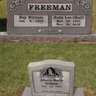Two grave markers on grass: a large Freeman family headstone behind a smaller individual headstone for Alberta Marie Gilson.