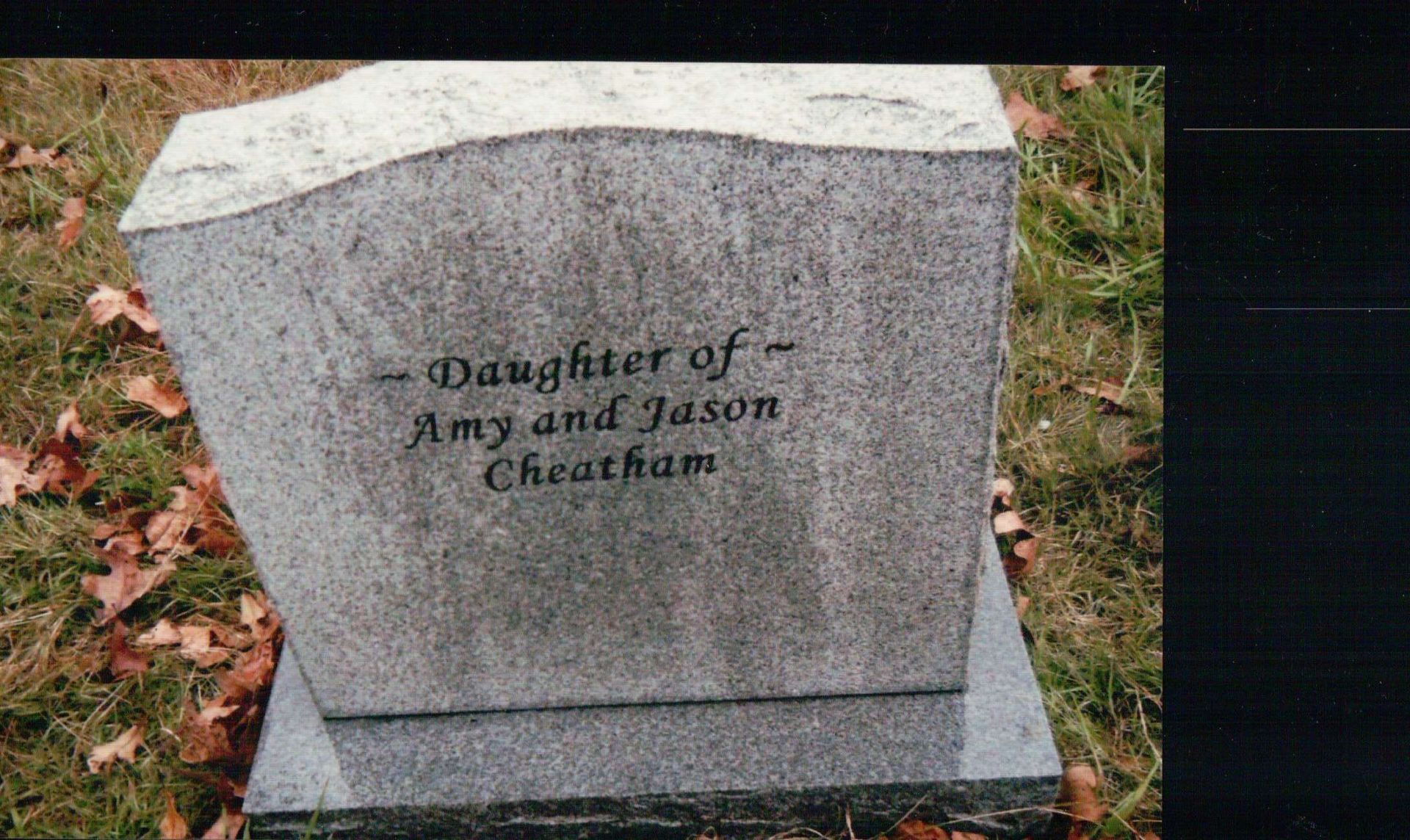 A gray granite headstone on grass with the inscription, 