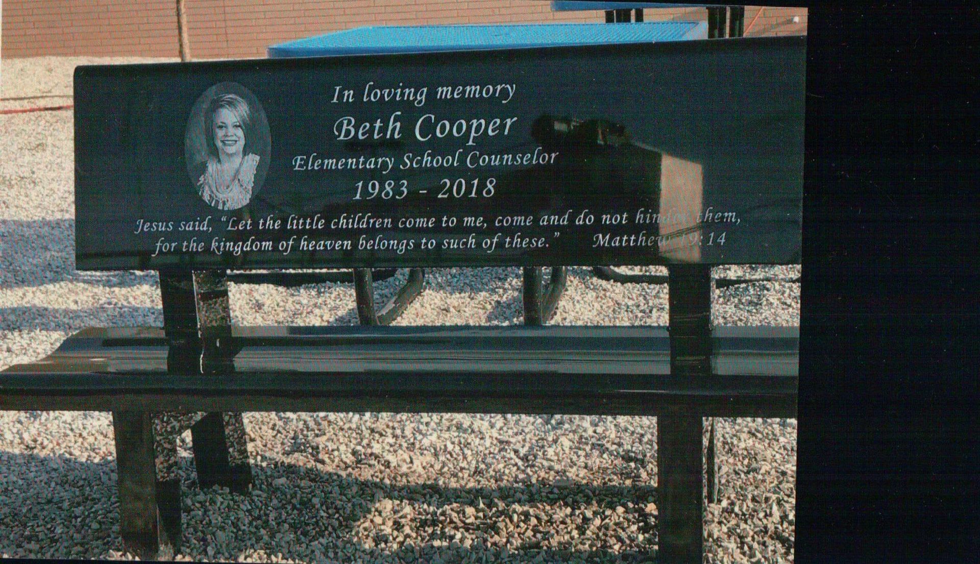 A memorial bench for Beth Cooper, an elementary school counselor, featuring her photo and a Bible verse inscription.