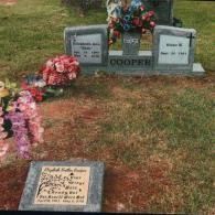 A grey granite double headstone for the Cooper family with flowers, and a smaller, separate headstone in the foreground.