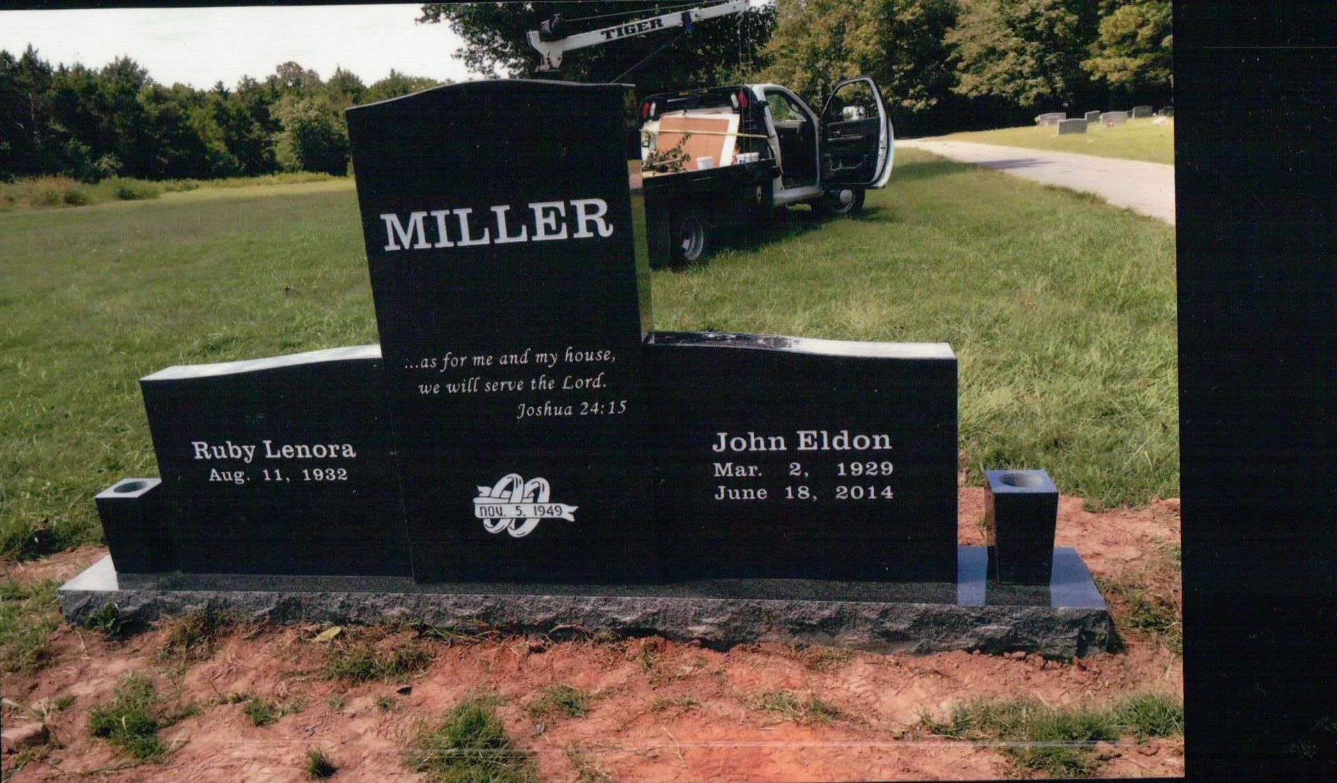 A black granite double headstone for the Miller family, set in a grassy cemetery with a utility truck in the background.