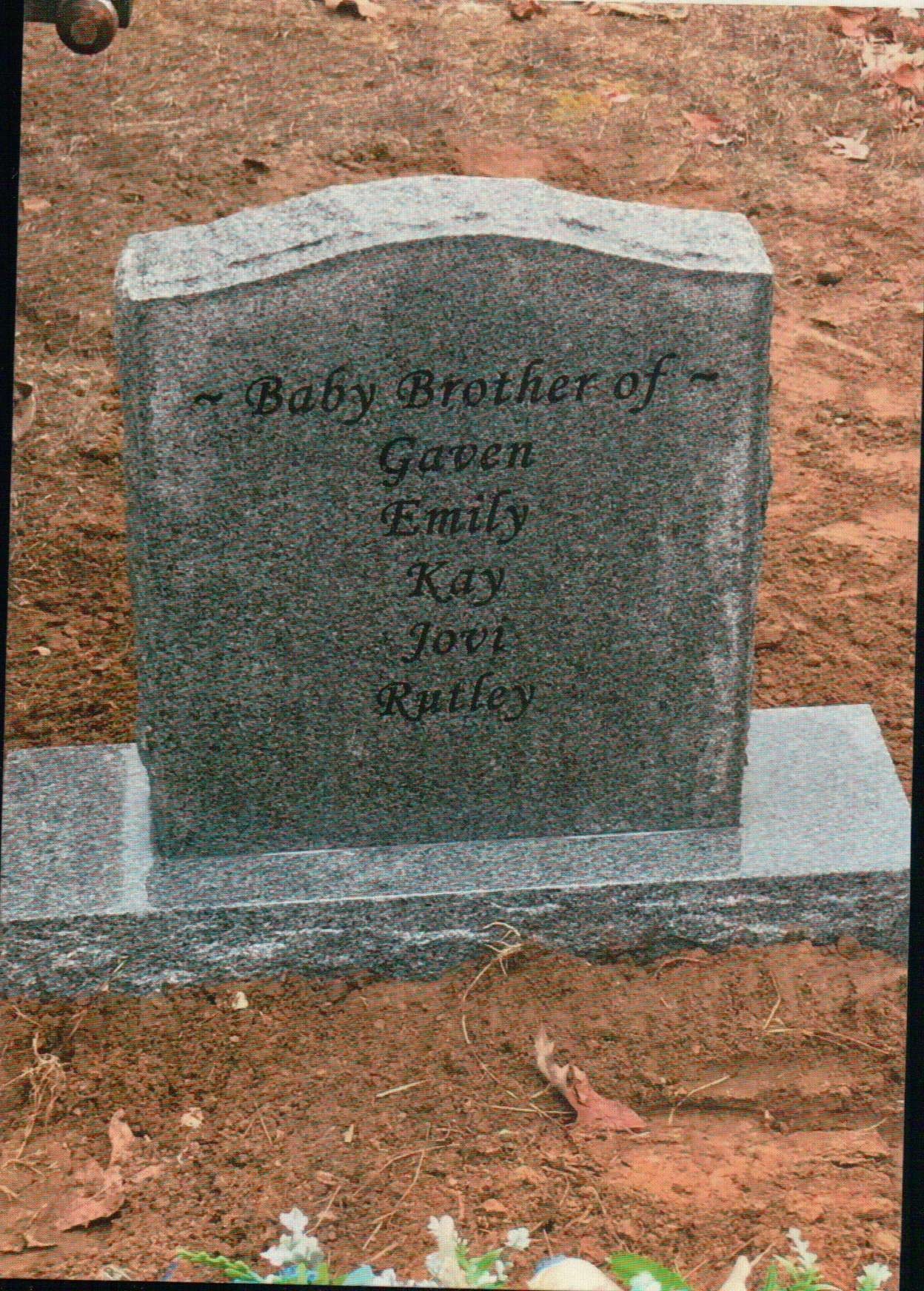 A grey, upright granite headstone set in reddish dirt, engraved with the words 