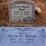 Two gravestones in a cemetery: one for Ernie Wayne Neal (1943-2016) with a dog and car, and one for Gary D. Riley (1950-2017).