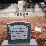 A grey granite headstone for Donnie Ray Williams, inscribed with dates and symbols, in a cemetery with other markers.
